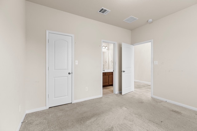 unfurnished bedroom featuring light colored carpet and ensuite bath