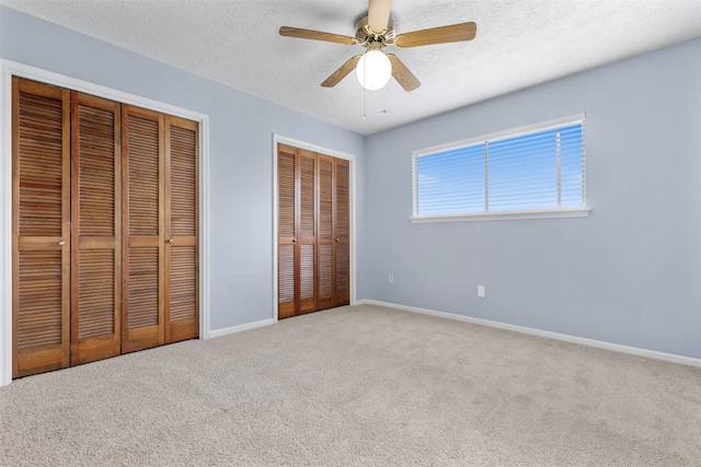 unfurnished bedroom with multiple closets, ceiling fan, carpet floors, and a textured ceiling