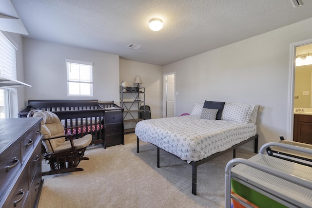 bedroom with visible vents, light carpet, a textured ceiling, and ensuite bathroom