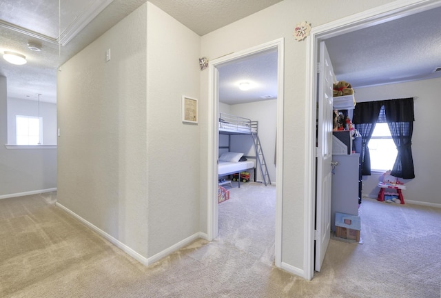 hall with a textured ceiling, carpet, attic access, and baseboards