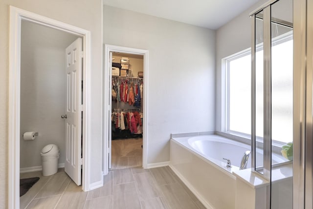 full bathroom featuring a stall shower, baseboards, a walk in closet, and a bath