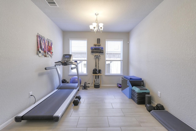 workout area featuring a textured wall, visible vents, a notable chandelier, and baseboards