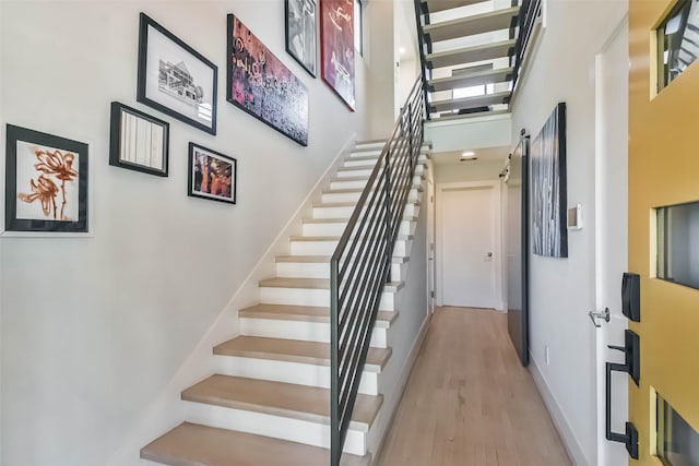 stairway with a high ceiling, wood-type flooring, and a barn door