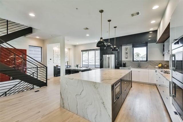 kitchen featuring a kitchen island, appliances with stainless steel finishes, pendant lighting, white cabinetry, and light hardwood / wood-style floors