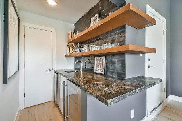 bar featuring sink, light hardwood / wood-style flooring, dark stone countertops, wine cooler, and decorative backsplash