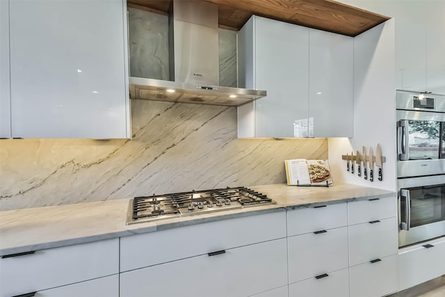 kitchen featuring wall chimney range hood, backsplash, stainless steel appliances, and white cabinets