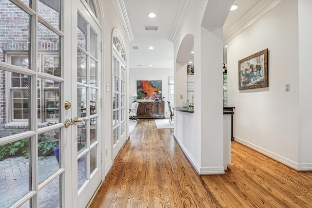 hall featuring ornamental molding, light hardwood / wood-style floors, a healthy amount of sunlight, and french doors