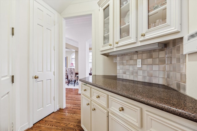 kitchen featuring decorative backsplash, dark wood-type flooring, dark stone counters, and vaulted ceiling