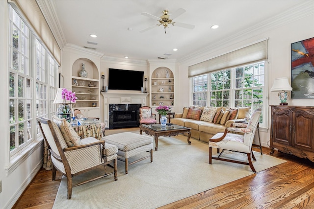 living room with crown molding, a fireplace, built in shelves, and hardwood / wood-style flooring