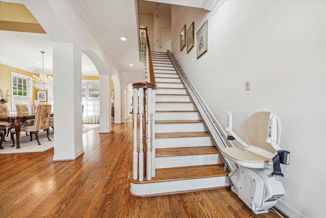 staircase with ornamental molding, wood-type flooring, and a chandelier