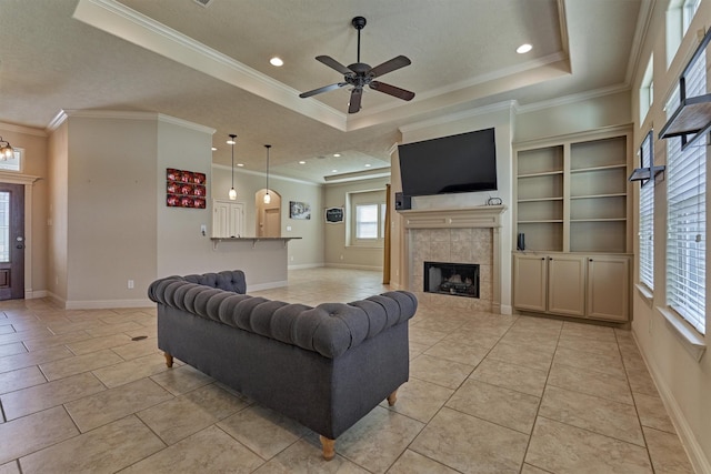 living room featuring a tile fireplace, light tile patterned floors, ceiling fan, a raised ceiling, and crown molding