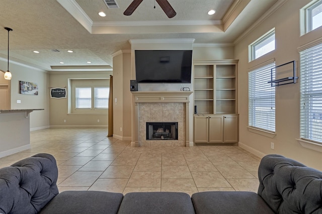 tiled living room featuring a tray ceiling, ornamental molding, a tile fireplace, and ceiling fan