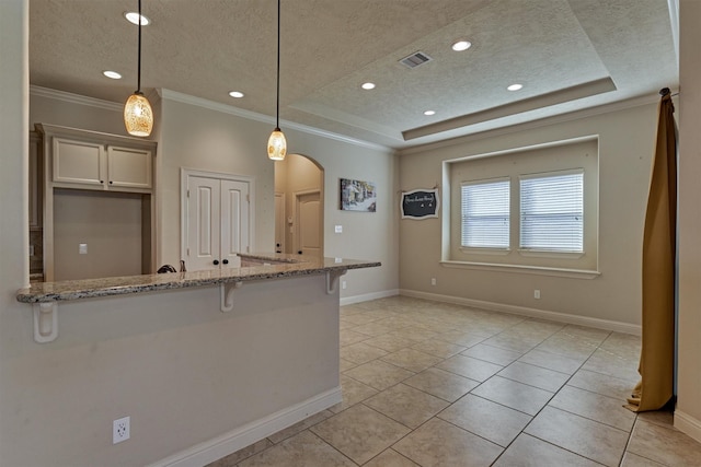 kitchen with hanging light fixtures, light stone countertops, a raised ceiling, and white cabinets