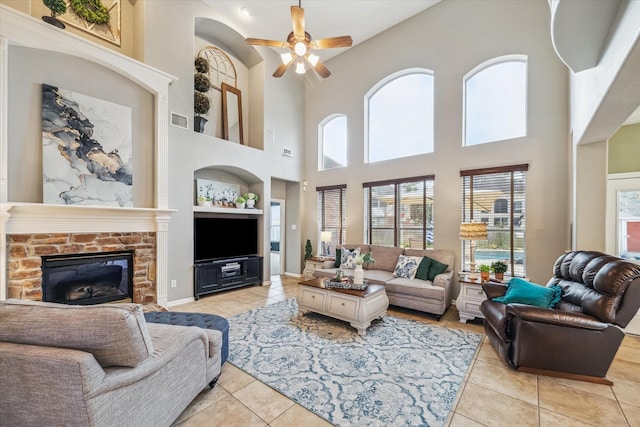 living room featuring ceiling fan, a stone fireplace, built in features, and light tile patterned floors