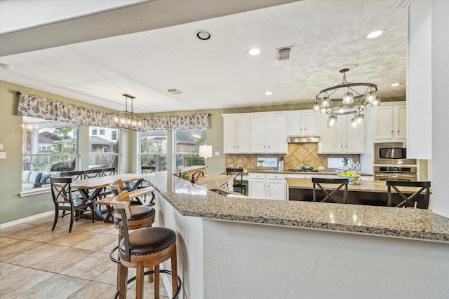 kitchen with a breakfast bar, tasteful backsplash, appliances with stainless steel finishes, pendant lighting, and white cabinets