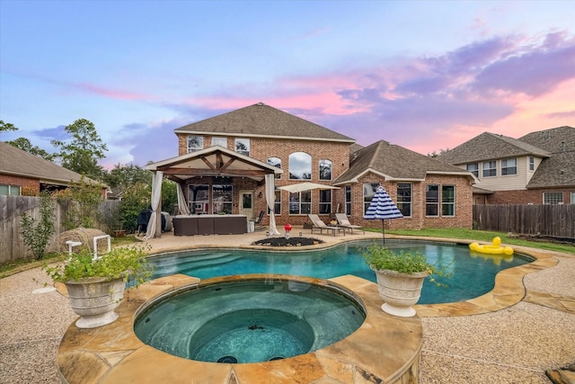 pool at dusk featuring an in ground hot tub, outdoor lounge area, and a patio area