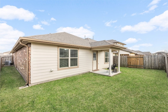 rear view of property featuring central AC unit, a fenced backyard, brick siding, a shingled roof, and a yard