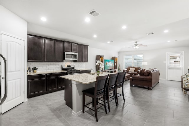 kitchen with a center island with sink, appliances with stainless steel finishes, open floor plan, a breakfast bar area, and a sink