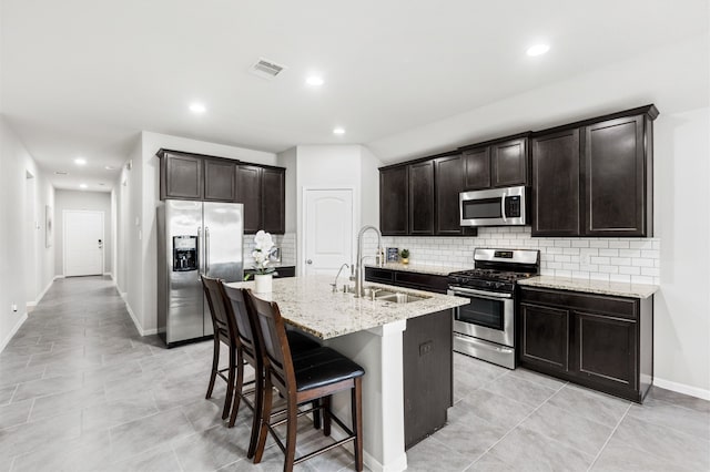 kitchen featuring a center island with sink, visible vents, appliances with stainless steel finishes, a sink, and a kitchen bar