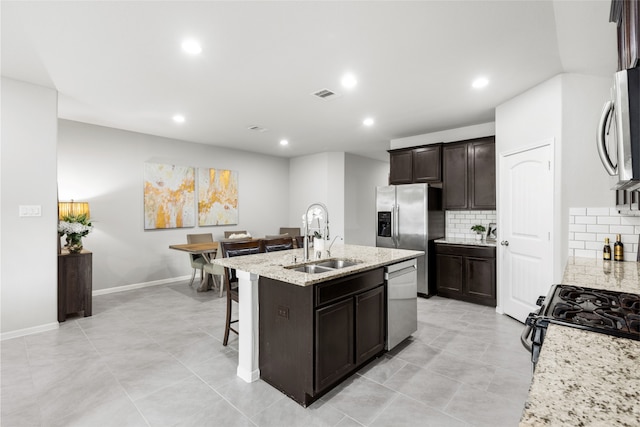 kitchen with stainless steel appliances, a sink, visible vents, light stone countertops, and a center island with sink