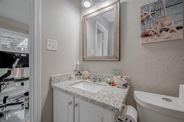 half bath featuring toilet, vanity, and a textured wall