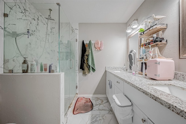 full bath featuring double vanity, a marble finish shower, baseboards, marble finish floor, and a sink