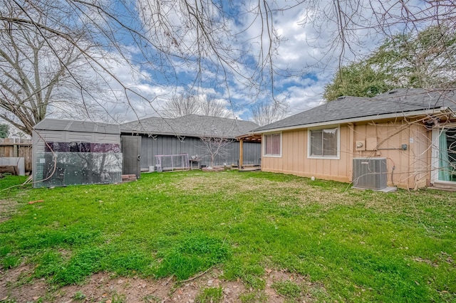 rear view of house featuring fence, an outdoor structure, central AC, and a yard