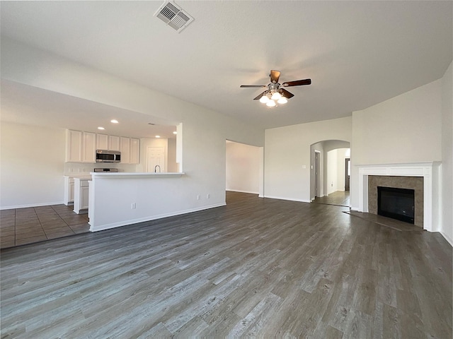 unfurnished living room featuring dark wood-type flooring, ceiling fan, and a tile fireplace