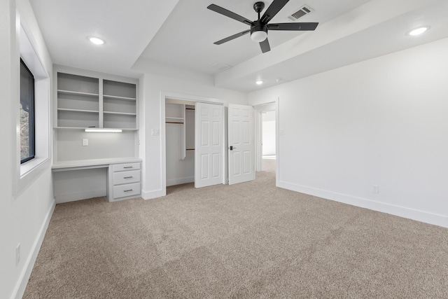 unfurnished bedroom featuring light carpet, built in desk, and ceiling fan