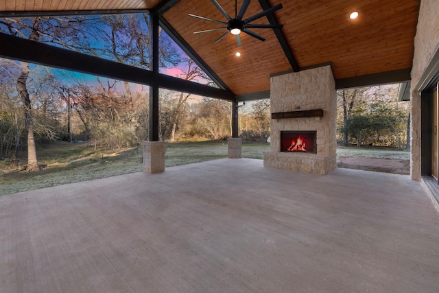 patio terrace at dusk featuring ceiling fan and an outdoor stone fireplace