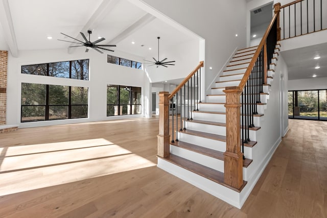 stairs with ceiling fan, beam ceiling, a towering ceiling, wood-type flooring, and a wealth of natural light