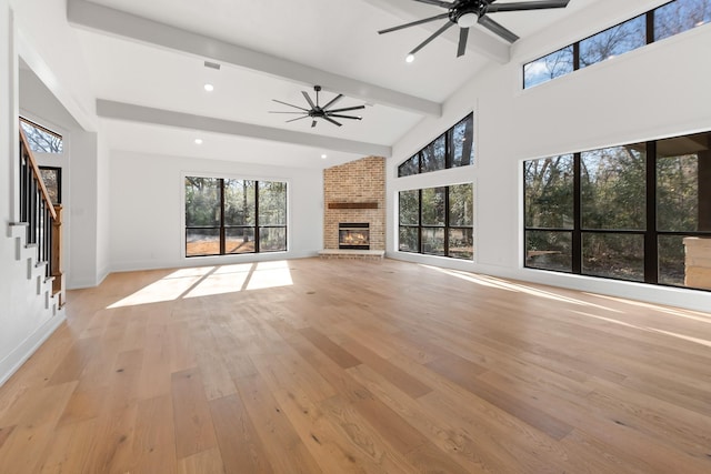 unfurnished living room featuring a fireplace, high vaulted ceiling, ceiling fan, beam ceiling, and light hardwood / wood-style floors