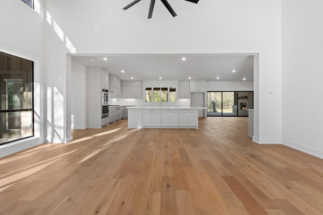 unfurnished living room featuring sink, light wood-type flooring, and a high ceiling