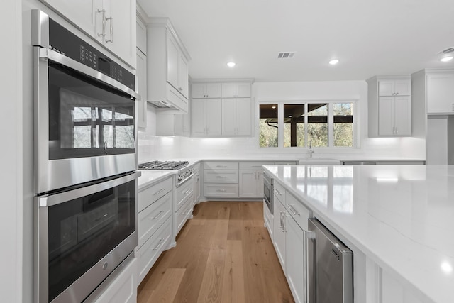 kitchen featuring wine cooler, white cabinets, light stone counters, light hardwood / wood-style floors, and stainless steel appliances