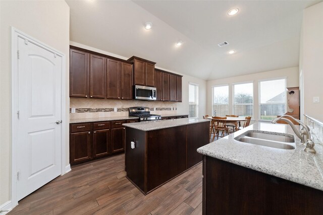 kitchen with stainless steel appliances, a kitchen island, a sink, visible vents, and vaulted ceiling