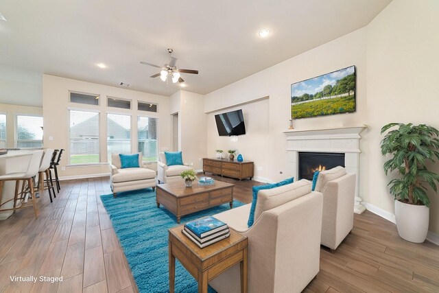 living room with a ceiling fan, a warm lit fireplace, baseboards, and wood finished floors