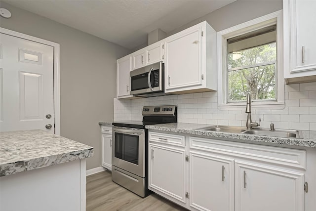 kitchen with sink, appliances with stainless steel finishes, white cabinetry, decorative backsplash, and light wood-type flooring