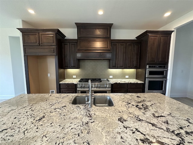 kitchen featuring appliances with stainless steel finishes, sink, backsplash, light stone counters, and dark brown cabinets