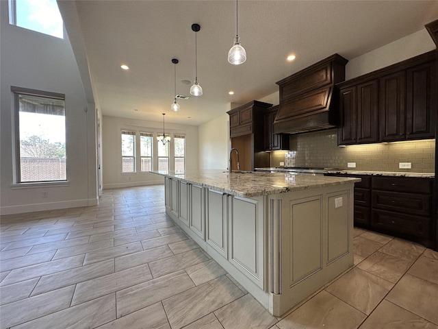 kitchen featuring premium range hood, dark brown cabinetry, decorative light fixtures, a large island, and light stone countertops