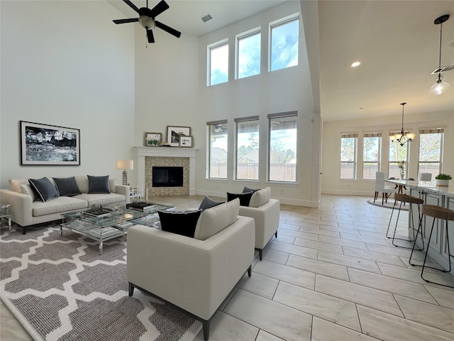 living room featuring light tile patterned floors, ceiling fan with notable chandelier, a fireplace, and a towering ceiling