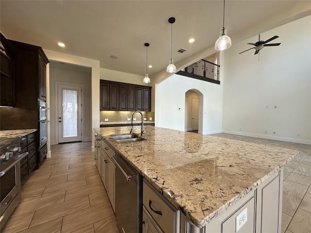 kitchen featuring sink, a kitchen island with sink, light stone counters, decorative backsplash, and stainless steel dishwasher