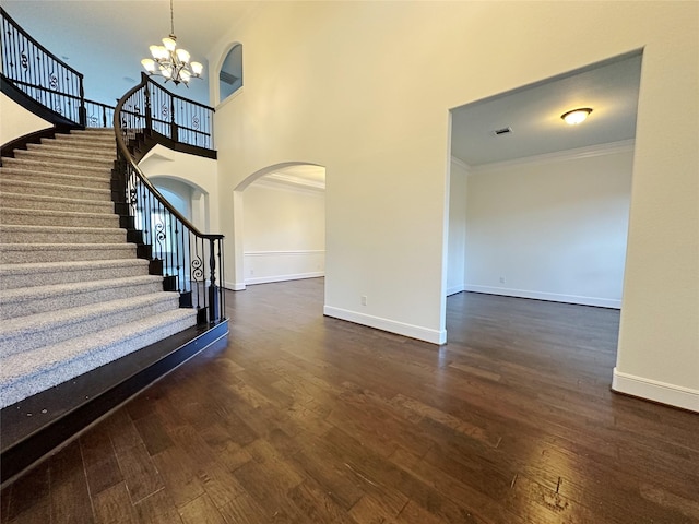 foyer entrance with a high ceiling, ornamental molding, dark wood-type flooring, and a notable chandelier