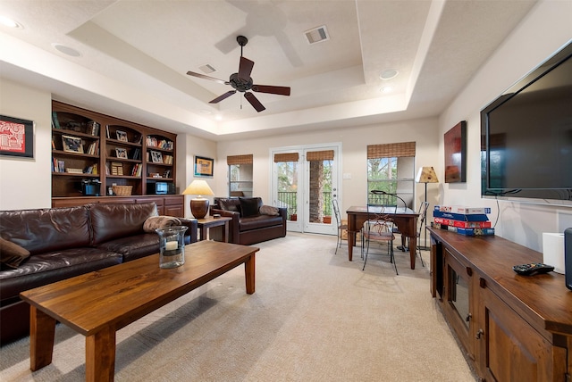 carpeted living room with a tray ceiling, french doors, and ceiling fan