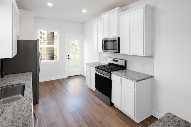 kitchen featuring sink, appliances with stainless steel finishes, white cabinetry, backsplash, and light stone counters