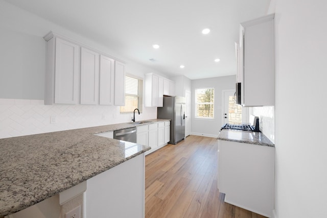 kitchen featuring appliances with stainless steel finishes, sink, white cabinets, light stone countertops, and light wood-type flooring