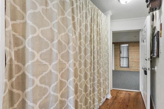 corridor featuring ornamental molding, wood-type flooring, a textured ceiling, and wood walls