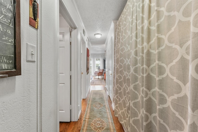 hall with hardwood / wood-style flooring, ornamental molding, and a textured ceiling