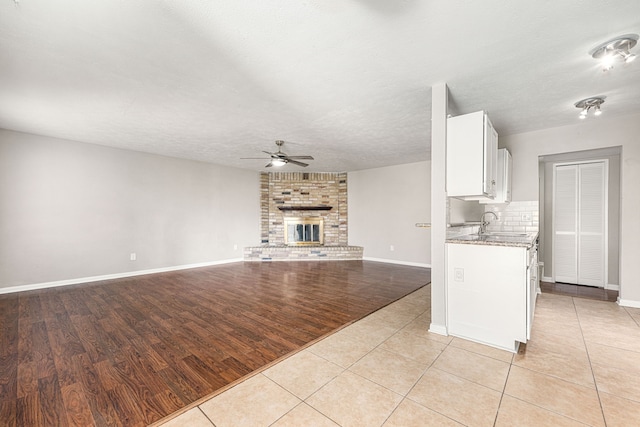 kitchen featuring stone countertops, a brick fireplace, light tile patterned floors, ceiling fan, and white cabinets