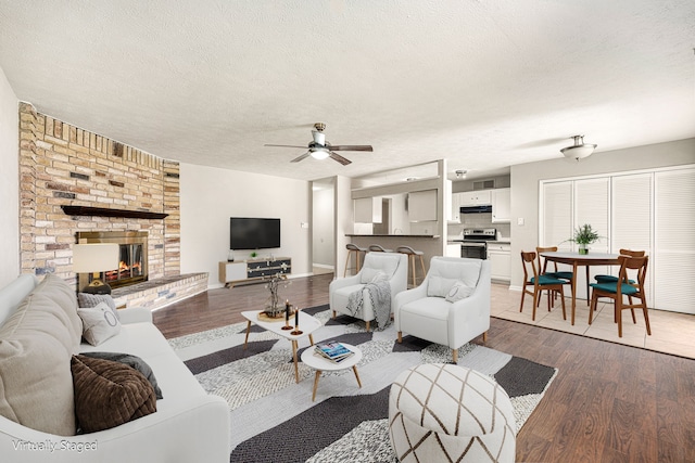 living room featuring hardwood / wood-style floors, a textured ceiling, a brick fireplace, and ceiling fan