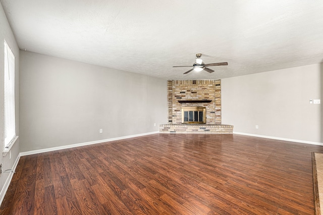 unfurnished living room with ceiling fan, dark hardwood / wood-style flooring, a brick fireplace, and a textured ceiling